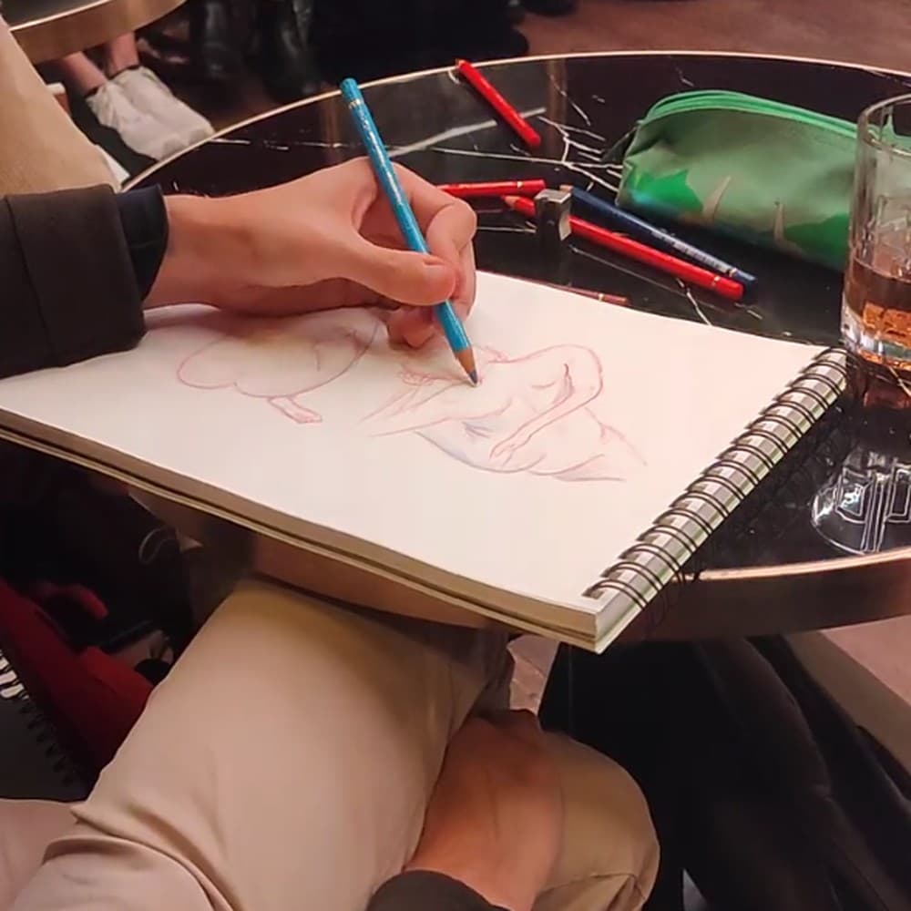 Une main esquisse un modèle au crayon, un verre posé sur la table